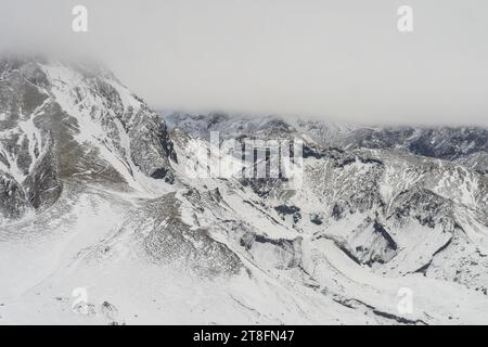 Aus dem dicken Winternebel erhebt sich ein Blick aus der Vogelperspektive auf die schneebedeckten Berggipfel Stockfoto