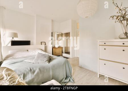 Komfortables Bett mit Blumenvase auf Kommode im geräumigen Schlafzimmer mit weißen Wänden in einem modernen Apartment Stockfoto