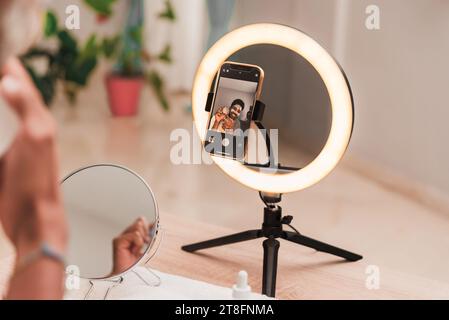 Eine Einzelperson nimmt sich auf einem Smartphone auf, das auf einem Ringlichtständer montiert ist, und zeigt eine moderne Einrichtung zur Inhaltserstellung. Stockfoto