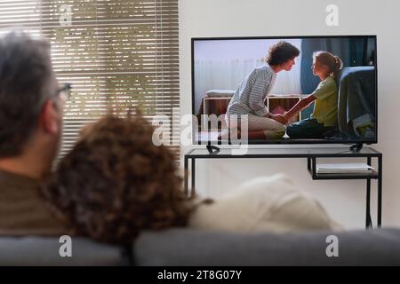 Rückansicht eines Paares, das auf dem Sofa sitzt und sich umschließt, während es zu Hause gemeinsam einen Film ansieht Stockfoto
