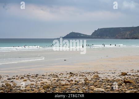 Menschen surfen am Strand von Sennen nahe Land's End in Cornwall, mit den Klippen von Cape Cornwall in der Ferne. Stockfoto