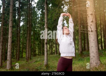 Sportliche Frau, die Dehnübungen im Wald macht, Aufwärmübungen macht. Stockfoto