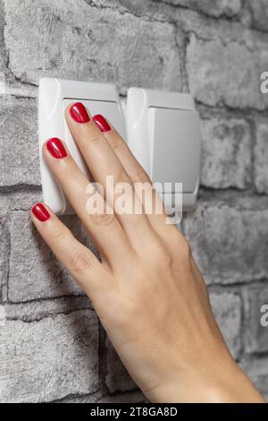 Die Frau macht das Licht im Raum an. Die Hand der Frau drückt den Lichtschalter. Stockfoto