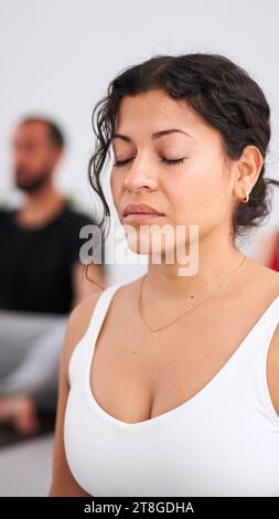 Close-up junge Latina Frau mit geschlossenen Augen beim Praktizieren von Yoga-Übungen in Innenräumen. Gruppe von Personen Stockfoto