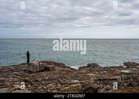 Ein Fischer steht auf einem Felsvorsprung am Ufer von Portland Bill an der Jurassic Coast von Dorset. Stockfoto