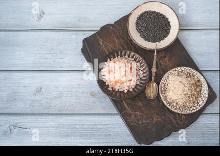 Verschiedene Salzsorten. Drei verschiedene Salzsorten in handgefertigten Tellern auf einer Tonplatte. Weißes Kräutersalz, rosa Himalaya und schwarz Stockfoto