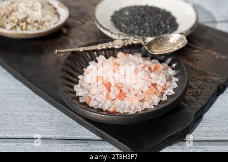 Verschiedene Salzsorten. Drei verschiedene Salzsorten in handgefertigten Tellern auf einer Tonplatte. Weißes Kräutersalz, rosa Himalaya und schwarz Stockfoto