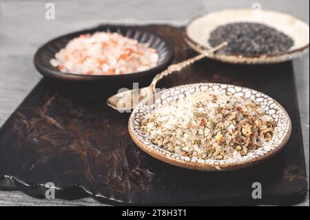 Verschiedene Salzsorten. Drei verschiedene Salzsorten in handgefertigten Tellern auf einer Tonplatte. Weißes Gewürzsalz, rosafarbenes Himalaya-Salz und schwarzer Maldon Stockfoto