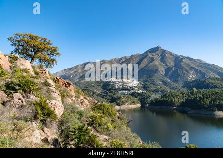 Ein Blick von einer Klippe mit Blick auf einen Stausee und Pueblo Blanco am Fuße eines Berges entlang der Costa del Sol. Stockfoto