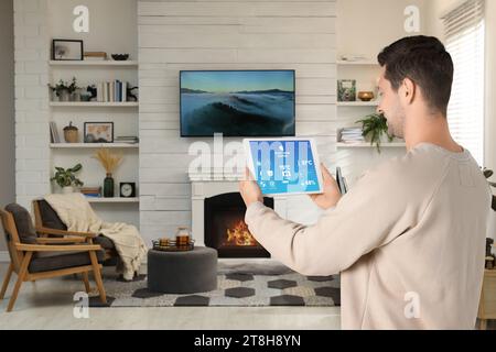 Mann, der das Smart Home Control System über Anwendung auf Tablet in Innenräumen verwendet Stockfoto