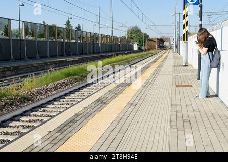 Ein junges Mädchen wartet, bis der Zug an der Haltestelle im Freien ankommt, während er in Italien telefoniert Stockfoto