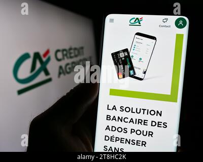 Person, die ein Mobiltelefon mit Webseite des französischen Finanzdienstleisters Crédit Agricole S.A. mit Logo hält. Konzentrieren Sie sich auf die Mitte des Telefondisplays. Stockfoto