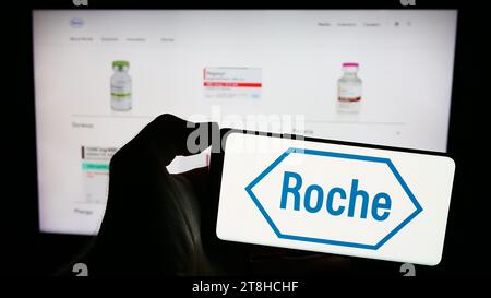 Person mit Mobiltelefon mit Logo des Schweizer Gesundheitsunternehmens Roche Holding AG vor der Business-Webseite. Schwerpunkt auf dem Display des Telefons. Stockfoto