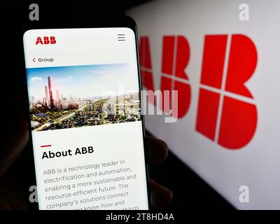 Person, die ein Mobiltelefon hält, mit Webseite des Elektrogeräteunternehmens ABB Ltd. Vor dem Firmenlogo. Konzentrieren Sie sich auf die Mitte des Telefondisplays. Stockfoto