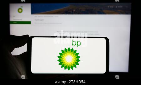 Person, die ein Mobiltelefon mit dem Logo des britischen Erdölunternehmens BP plc vor der Webseite hält. Schwerpunkt auf dem Display des Telefons. Stockfoto