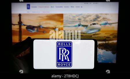 Person, die ein Smartphone mit dem Logo des britischen Luftfahrtunternehmens Rolls-Royce Holdings plc vor der Website hält. Schwerpunkt auf dem Display des Telefons. Stockfoto