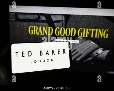 Person mit Smartphone und Logo des britischen Bekleidungsunternehmens Ted Baker plc vor der Website. Schwerpunkt auf dem Display des Telefons. Stockfoto