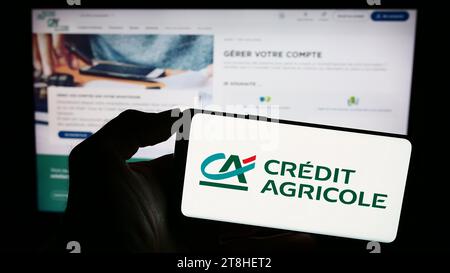 Person mit Smartphone und Logo des französischen Finanzdienstleisters Crédit Agricole S.A. vor der Website. Schwerpunkt auf dem Display des Telefons. Stockfoto