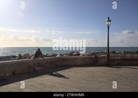 Mann sitzt auf einem Betongeländer am Wellenbrecher an einem sonnigen Tag am Meer Stockfoto