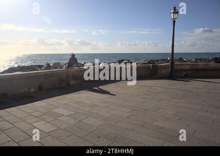 Mann sitzt auf einem Betongeländer am Wellenbrecher an einem sonnigen Tag am Meer Stockfoto