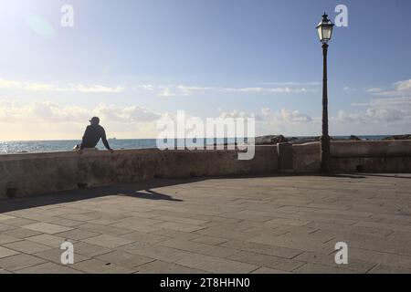 Mann sitzt auf einem Betongeländer am Wellenbrecher an einem sonnigen Tag am Meer Stockfoto