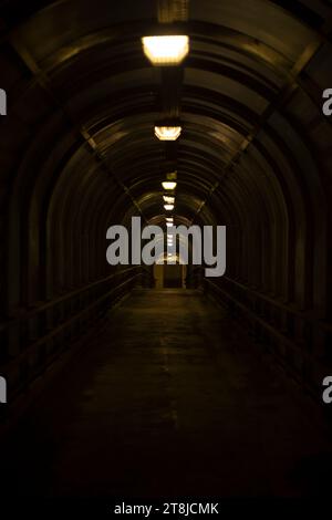 Tunnel im Dunkeln. Fußgänger überqueren einen Tunnel über der Straße. Langer Korridor. Verkehrsinfrastruktur. Stockfoto