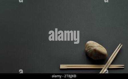 Japanische Bambusstäbchen und heller Stein auf dunkelgrauem Hintergrund. Minimalismus, Komposition in einer Ecke, großer Kopierraum Stockfoto