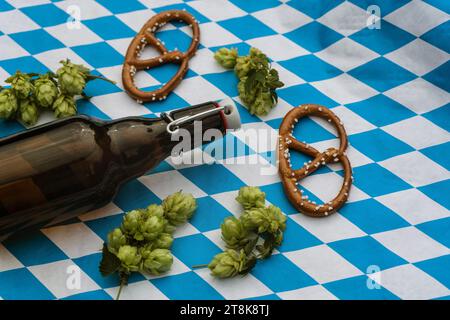 Gewöhnlicher Hopfen (Humulus lupulus), Flaschenbier und Hopfenkegel und Brezn auf bayerischer Flagge, Deutschland, Bayern Stockfoto