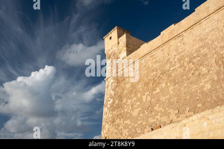 Nahaufnahme der hohen Mauer der historischen Zitadelle auf Gozo in Malta. Die starken Mauern ragen hoch. Der Himmel ist blau mit hellen Wolken. Stockfoto