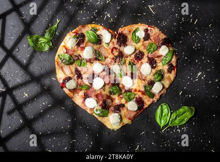 Köstliche und knusprige rote Frucht-Pizza in Herzform mit Basilikum Stockfoto