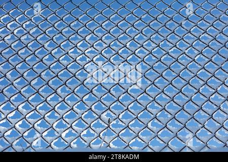 Schnee auf dem Maschendrahtzaun gegen den blauen Himmel Stockfoto