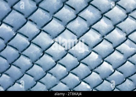 Schnee auf dem Maschendrahtzaun gegen den blauen Himmel Stockfoto