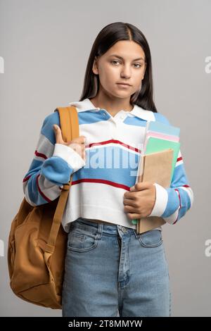 Teenager-Mädchen mit Rucksack und Notizbüchern. Ernsthaftes, unlächelndes Mädchen in selbstbewusster Pose, das in die Kamera schaut Stockfoto