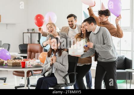 Eine Gruppe von Geschäftsleuten, die ihren Kollegen auf einer Party im Büro mit einem Geburtstagskuchen überraschen Stockfoto