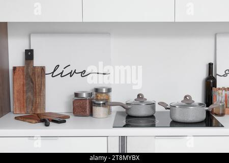 Weiße Küchenzeile mit Elektroherd, Töpfen und Besteck Stockfoto