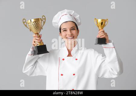 Weibliche Köchin mit goldenen Tassen auf hellem Hintergrund Stockfoto