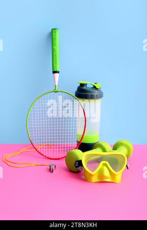 Badmintonschläger mit Kurzhanteln, Schwimmbrille und Sportflasche auf farbenfrohem Hintergrund Stockfoto