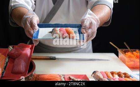 Ein erfahrener Sushi-Koch präsentiert stolz einen wunderschön angeordneten Teller mit köstlichem Sushi und demonstriert die Kunstfertigkeit und Präzision der Kuli Stockfoto