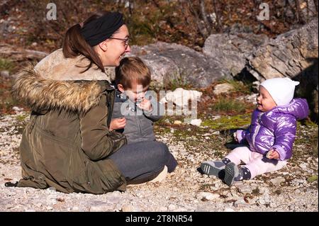 Mutter mit Kleinkind und Mädchen, die in der Natur auf dem Boden sitzen Stockfoto