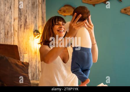 Mutter, die in den Armen einen Jungen aufzieht, der auf dem Bett in einem Hotel sitzt Stockfoto