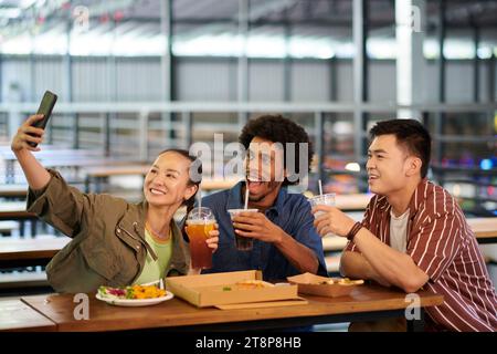 Fröhliche, vielfältige Gruppe von Freunden, die beim gemeinsamen Mittagessen im Café Selfie machen Stockfoto