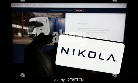 Person, die ein Mobiltelefon mit dem Logo des amerikanischen Elektrofahrzeugunternehmens Nikola Corporation vor der Webseite hält. Schwerpunkt auf dem Display des Telefons. Stockfoto
