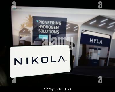Person, die ein Mobiltelefon mit dem Logo des US-amerikanischen Elektrofahrzeugunternehmens Nikola Corporation vor der Website des Unternehmens hält. Schwerpunkt auf dem Display des Telefons. Stockfoto