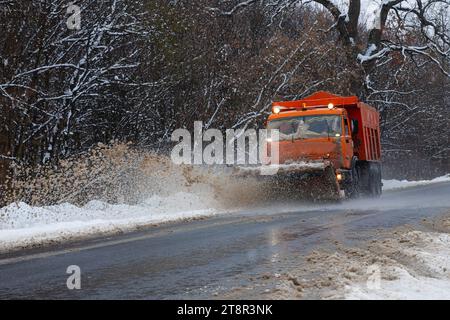 Ein großes Auto mit einem Pflug befreit die Straße von Schnee. Die Sonderausrüstung Orange Cargo kämpft im Winter mit den Elementen. Beseitigung der Auswirkungen von t Stockfoto