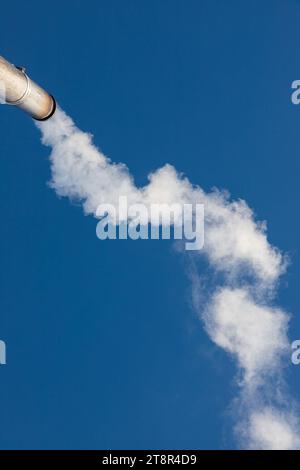 Eine Rauchfahne oder Dampf aus einem industriellen Schornstein an einem klaren blauen Himmel. Stockfoto