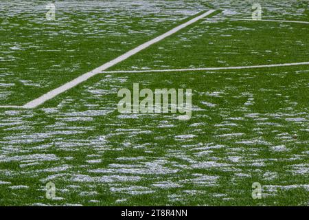 Das Fußballfeld mit Kunstrasen ist mit einer leichten Schneeschicht bedeckt. Frühling. Grünes Gras auf dem Fußballfeld ist von zu sehen Stockfoto