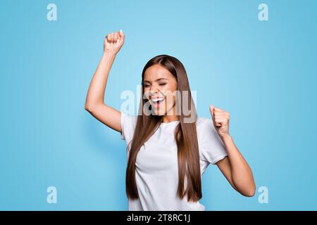 Porträt einer braunhaarigen, attraktiven, netten, aufgeregten jungen Dame, die den Sieg feiert, vor grauem Hintergrund, isoliert Stockfoto