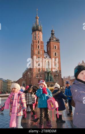 Kinder spielen mit Tauben vor der St. Marienkirche im Winter auf dem Hauptmarkt in Krakau, Polen Stockfoto