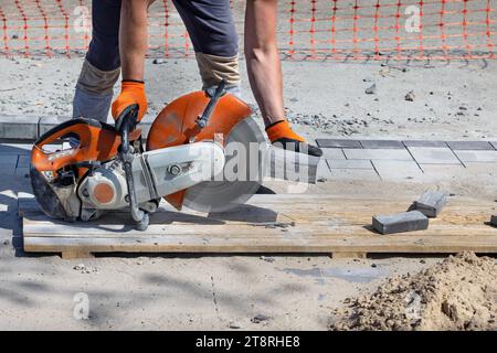 Schneiden von Pflasterplatten beim Verlegen mit einer Säge und einer Diamantklinge. Ein suspendierter Arbeiter schneidet einen Steinblock. Kopierbereich. Stockfoto