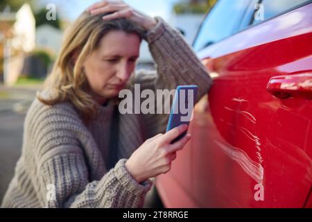 Unglückliche Reife Weibliche Fahrerin, Die Ein Foto Von Schäden Am Auto Nach Einem Unfall Auf Dem Handy Macht Stockfoto